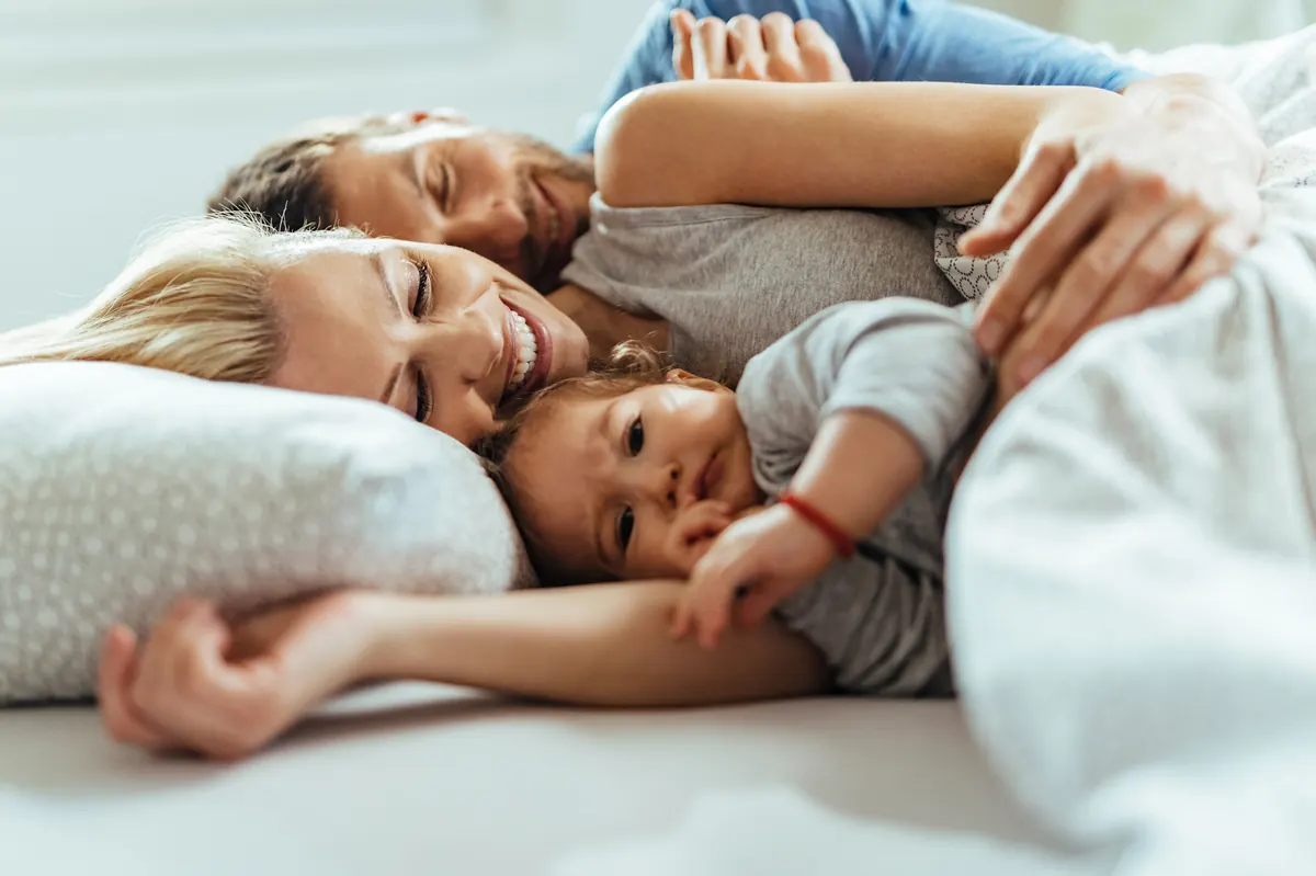 Familie mit Kleinkind liegt entspannt zusammen im Bett